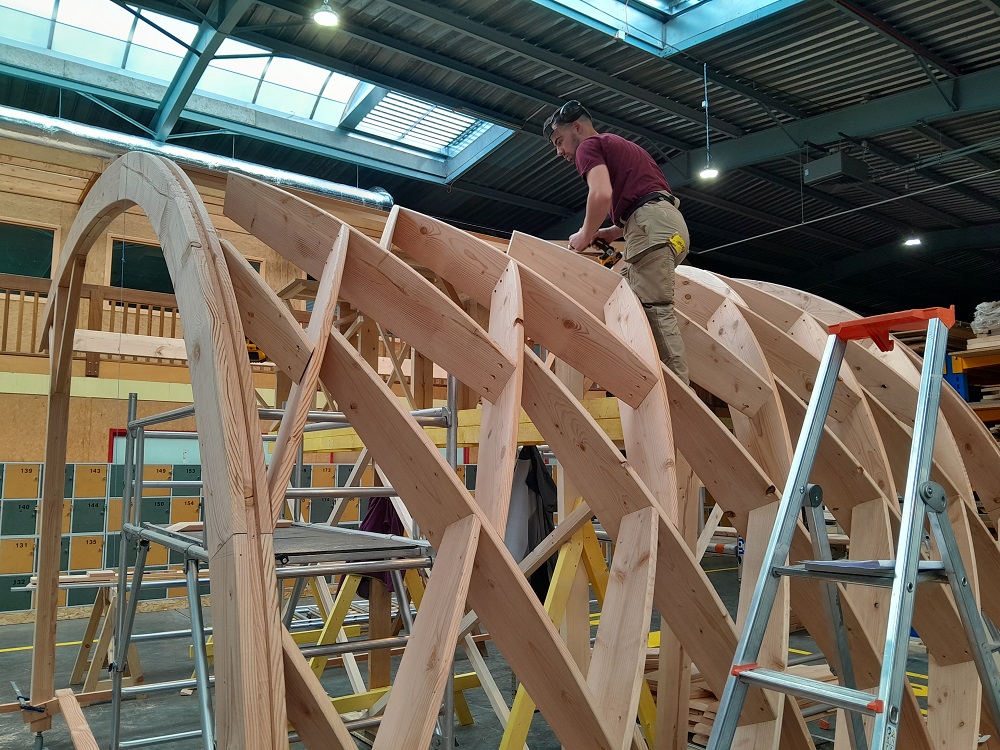 Etudiant sur une structure en bois dans la halle de l'ENSTIB